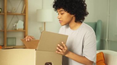 Paketleri açan Afrikalı kız kutuya bakıyor. Kutuyu açan mutlu kadın. Paket teslim edilen eşyalara bakan bir kadın. Tatmin olmuş istemci olumlu geri bildirim hızlı teslimatı