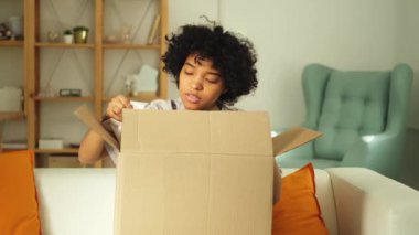 Paketleri açan Afrikalı kız kutuya bakıyor. Kutuyu açan mutlu kadın. Paket teslim edilen eşyalara bakan bir kadın. Tatmin olmuş istemci olumlu geri bildirim hızlı teslimatı