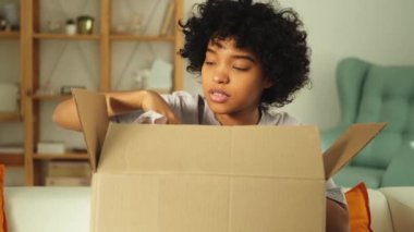 Paketleri açan Afrikalı kız kutuya bakıyor. Kutuyu açan mutlu kadın. Paket teslim edilen eşyalara bakan bir kadın. Tatmin olmuş istemci olumlu geri bildirim hızlı teslimatı