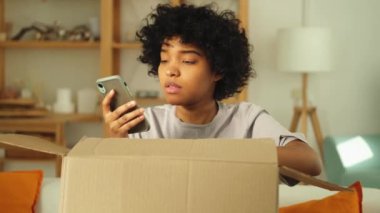 Mutsuz kızgın Afrikalı kadın posta servisinde arızalı nakliye hatasıyla gelen kutuyu açıyor. Sinirli müşteri istemcisi akıllı telefondan yanlış paket kontrolü uygulaması alıyor