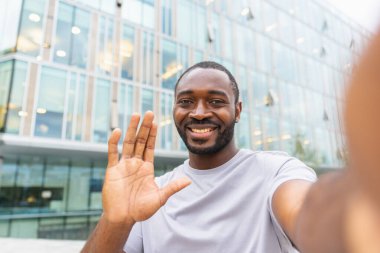 Akıllı telefonlu Afro-Amerikalı bir adam şehirde video görüşmesi yapıyor. Blogcu adam sosyal ağda sohbet ediyor. Adamın sanal toplantı vlog 'u açık havada Selfie web kamerası görüntüsü var