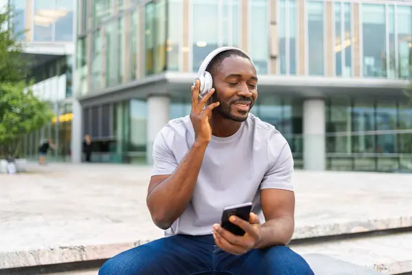 stock image Music song concept. Good start day. Happy African American man listening modern hit on street in city. Person guy wearing headphones enjoy listening favorite music on phone. People lifestyle joy