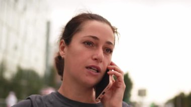 Açık havada, sokakta akıllı telefondan konuşan genç bir kadın. Cep telefonlu bir kız arkadaşlarıyla sohbet ediyor. Gülümseyen kişi cep telefonuyla cevap veriyor. Cep telefonuyla konuşan kadın