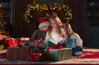 Mutlu Noeller Noel tatili. Çocuklar Noel ağacının yanındaki hediye kutusunu açıyor. Oturma odasında Noel ağacı şöminesi olan çocuklar sürpriz yüzlü hediye kutusunu açıyorlar. Evde Noel arifesi