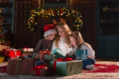 Mutlu Noeller Noel tatili. Çocuklar Noel ağacının yanındaki hediye kutusunu açıyor. Oturma odasında Noel ağacı şöminesi olan çocuklar sürpriz yüzlü hediye kutusunu açıyorlar. Evde Noel arifesi