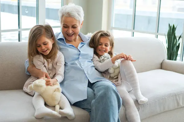 stock image Happy family at home. Two little girls sisters twins grandmother enjoying time together. Good time at home. Grandma granddaughters child kids emotional bonding hugging together. Family generations