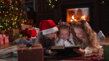 Mutlu Noeller Noel tatili. Erkek kardeşler çocuklar çocuklar Noel ağacının yanında kış akşamı şömineli oturma odasında sihirli noel kitabı okuyorlar. Evde Noel arifesi