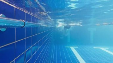 Profesyonel kadın yüzücünün sualtı görüntüsü. Yüzme havuzunda yüzen kadın sporcu. Sualtı manzaralı kadın havuza dalıyor. Suyun altında süzülen baloncuklarla süzülen kız görüntüsü