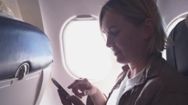Yolcu kadın uçakla geliyor. Uçak penceresinin yanında oturan telefonu kullanan bir kız. Uçuşun tadını çıkaran akıllı telefonlu gezgin bir kadın. Gemide kablosuz bağlantı kullanan bir kadın var. Gezgin kız.