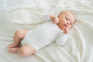 Mutlu bebek. Yatak odasında, gülümseyen yüzüyle küçük şirin bir kız. Bebek dinleniyor, evde beyaz battaniyeye uzanmış oynuyor. Annelik mutlu çocuk bakımı konsepti