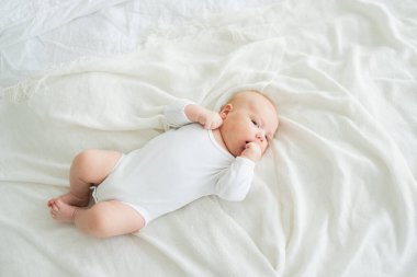 Mutlu bebek. Yatak odasında, gülümseyen yüzüyle küçük şirin bir kız. Bebek dinleniyor, evde beyaz battaniyeye uzanmış oynuyor. Annelik mutlu çocuk bakımı konsepti