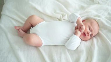 Mutlu bebek. Yatak odasında, gülümseyen yüzüyle küçük şirin bir kız. Bebek dinleniyor, evde beyaz battaniyeye uzanmış oynuyor. Annelik mutlu çocuk bakımı konsepti