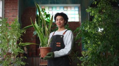 Kendi işimi yürütüyorum. Afrikalı çiçekçi kadın saksıda bitki tutuyor botanik mağazasında önlük giyiyor. Çiçekçide çalışan mutlu küçük işletme sahibi bitkilerle çevrili gülümsüyor. Küçük işletme