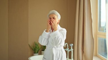 Yetişkin yaşlı bir kadın günlük güzellik rutini yaparak anti-yaş yüz kremi sürüyor. Yaşlı kadın cilt kırışıklıklarına dokununca yüz bakımı yaptırıyor. Yaşlanan cilt bakımı güzellik kozmetik ürünleri