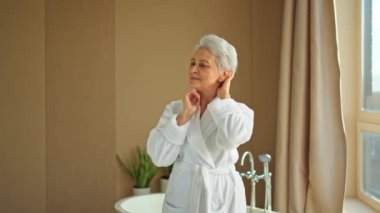 Yetişkin yaşlı bir kadın günlük güzellik rutini yaparak anti-yaş yüz kremi sürüyor. Yaşlı kadın cilt kırışıklıklarına dokununca yüz bakımı yaptırıyor. Yaşlanan cilt bakımı güzellik kozmetik ürünleri