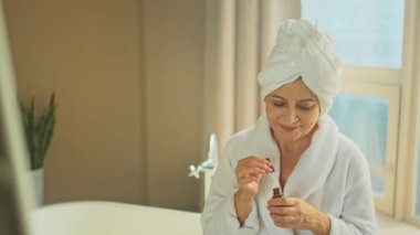 Cilde doğal damla kozmetik yağı süren bir kadın. Yetişkin yaşlı bir kadın günlük güzellik rutini yapan pipetli anti-yaş serumu uyguluyor. Yaşlı kadın yüz bakımı yaptırıyor.