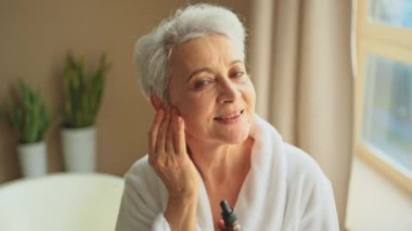 Cilde doğal damla kozmetik yağı süren bir kadın. Yetişkin yaşlı bir kadın günlük güzellik rutini yapan pipetli anti-yaş serumu uyguluyor. Yaşlı kadın yüz bakımı yaptırıyor.