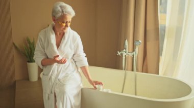 Olgun, yaşlı bir kadın ellerinde nemlendirici vücut losyonu sürüyor. Son sınıf öğrencisi kadın banyoda günlük cilt bakımını yaparken anti-yaş kremi sürüyor. Güzellik tedavisi vücut bakımını kapsar.