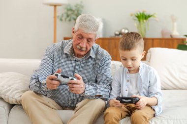 Mutlu bir aile. Yaşlı büyükbaba oğlan torun evde joysticklerle oyun oynuyor. Oyun için oyun bloknotları kullanarak gülümseyen büyükanne ve çocuk. Eski nesil modern teknoloji kullanımı