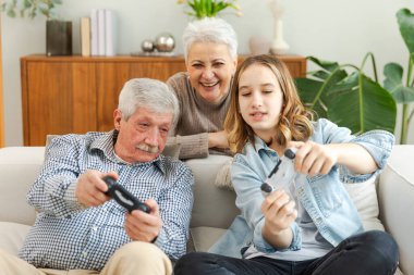 Evde mutlu bir aile. Yaşlı adam büyükbaba kadın büyükanne kız torun evde joysticklerle oyun oynuyor. Oyun için gamepad kullanan iki nesil büyükbaba ve ergen