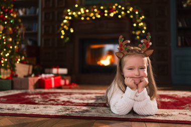 Mutlu noeller. Klasik karanlık iç mekanda Noel ağacının yanında gülümseyen küçük bir kız. Oturma odasında Noel ağacı hediye kutularıyla geyik boynuzu takan genç mutlu çocuk. Evde Noel arifesi