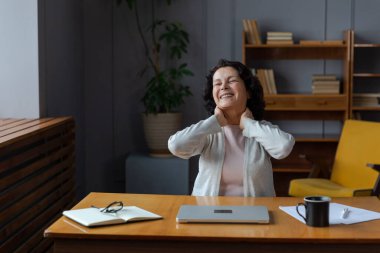 Orta yaşlı yaşlı bir kadın evde, ellerini ve vücudunu dinlendirip laptopta işe ara veriyor. Yaşlı, olgun bir kadın işten sonra mutlu olur. Uzun dizüstü bilgisayar kullanımından dolayı yorgunluk