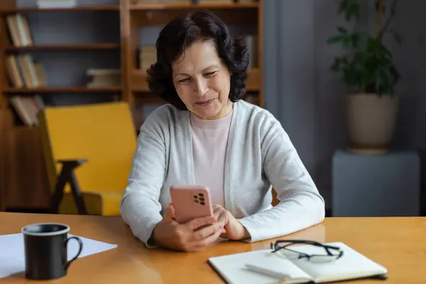 stock image European middle aged senior woman holding using smartphone touch screen typing scroll page. Stylish older mature 60s lady with cell phone using internet social media apps at home. Shopping online