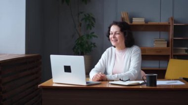 Orta yaşlı mutlu bir kadın dizüstü bilgisayarla oturup arkadaşlarıyla görüntülü konuşma yapıyor. Yaşlı ve olgun büyükanneme gülüp yetişkin çocuklarla internette konuşarak eğleniyorum.