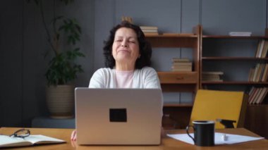 Orta yaşlı yaşlı bir kadın evde, ellerini ve vücudunu dinlendirip laptopta işe ara veriyor. Yaşlı, olgun bir kadın işten sonra mutlu olur. Uzun dizüstü bilgisayar kullanımından dolayı yorgunluk