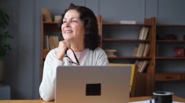 Evde dizüstü bilgisayar kullanan kendine güvenen Avrupalı orta yaşlı bir kadın. Yaşlı, şık 60 'lı yaşlarda bir kadın masada oturmuş bilgisayar ekranına bakıyor daktilo yazarak sohbet ediyor e-posta yazıyor.