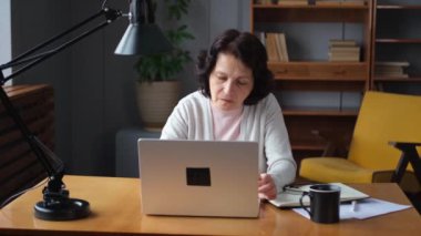 Evde dizüstü bilgisayar kullanan kendine güvenen Avrupalı orta yaşlı bir kadın. Yaşlı, şık 60 'lı yaşlarda bir kadın masada oturmuş bilgisayar ekranına bakıyor daktilo yazarak sohbet ediyor e-posta yazıyor.