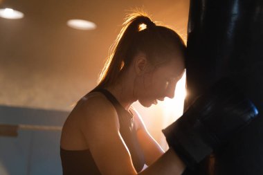 Kadın kendini savunma gücü. Boks ringinde dövüşten sonra dinlenen güçlü kadın boksör. Güçlü kız boks torbasını yumrukladıktan sonra yoruldu. Spor salonunda eğitim günü. Vücut çalıştırma eğitimine uygun güç