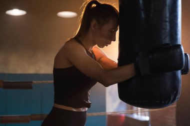 Kadın kendini savunma gücü. Boks ringinde dövüşten sonra dinlenen güçlü kadın boksör. Güçlü kız boks torbasını yumrukladıktan sonra yoruldu. Spor salonunda eğitim günü. Vücut çalıştırma eğitimine uygun güç