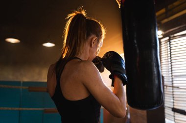 Kadın kendini savunma gücü. Güçlü kadın boks ringinde boks antrenmanı yapıyor. Sağlıklı, boks torbası yumruklayan güçlü bir kız. Boks salonunda antrenman günü. Vücut çalıştırma eğitimine uygun güç