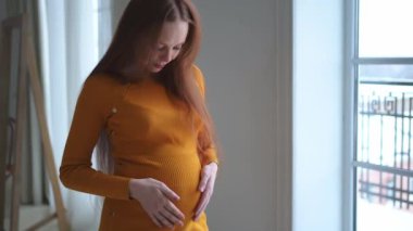 Hamilelik anneliği insanların gelecek beklentisi. Evinin penceresinin yanında koca göbekli hamile bir kadın var. Karnına sarılan ve hamileliğin tadını çıkaran bir kız. Annelik şefkati ebeveynlik yeni yaşam konsepti