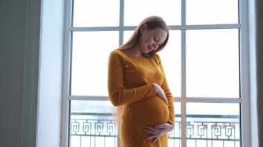 Hamilelik anneliği insanların gelecek beklentisi. Evinin penceresinin yanında koca göbekli hamile bir kadın var. Karnına sarılan ve hamileliğin tadını çıkaran bir kız. Annelik şefkati ebeveynlik yeni yaşam konsepti