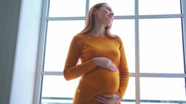 Hamilelik anneliği insanların gelecek beklentisi. Evinin penceresinin yanında koca göbekli hamile bir kadın var. Karnına sarılan ve hamileliğin tadını çıkaran bir kız. Annelik şefkati ebeveynlik yeni yaşam konsepti