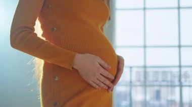 Hamilelik anneliği insanların gelecek beklentisi. Hamile kadın elleri pencerenin yanındaki koca göbeğe dokunuyor. Karnına sarılan ve hamileliğin tadını çıkaran bir kız. Annelik şefkati ebeveynlik yeni yaşam konsepti