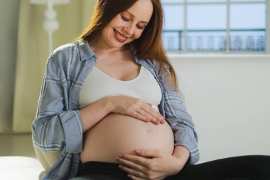 Hamilelik anneliği insanların gelecek beklentisi. Hamile bir kadın koca göbeğine dokunuyor. Evdeki koltukta oturuyor. Karnına sarılan ve hamileliğin tadını çıkaran bir kız. Annelik şefkati ebeveynlik yeni yaşam konsepti