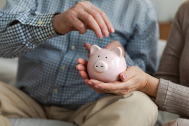 Gelecek için para yatırımı biriktiriyorum. Yaşlı yetişkin çift elleri domuz kumbarasına para koyuyor. Yaşlı kadın emeklilik bütçesinden tasarruf ediyor. Yatırım bankacılığı kavramı kaydediliyor
