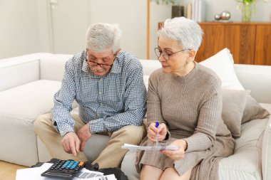 Orta yaşlı yaşlı çift dizüstü bilgisayarları ve kağıt belgeleriyle oturuyor. Yaşlı, olgun bir kadın kağıt faturası okuyor. Ev yöneticiliği yapıyor. Vergileri finanse ediyor.
