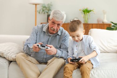 Mutlu bir aile. Yaşlı büyükbaba oğlan torun evde joysticklerle oyun oynuyor. Oyun için oyun bloknotları kullanarak gülümseyen büyükanne ve çocuk. Eski nesil modern teknoloji kullanımı