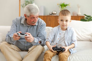 Mutlu bir aile. Yaşlı büyükbaba oğlan torun evde joysticklerle oyun oynuyor. Oyun için oyun bloknotları kullanarak gülümseyen büyükanne ve çocuk. Eski nesil modern teknoloji kullanımı