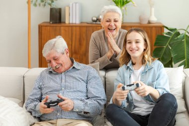 Evde mutlu bir aile. Yaşlı adam büyükbaba kadın büyükanne kız torun evde joysticklerle oyun oynuyor. Oyun için gamepad kullanan iki nesil büyükbaba ve ergen
