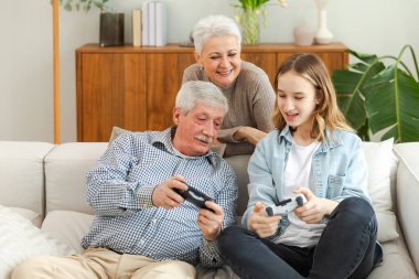 Evde mutlu bir aile. Yaşlı adam büyükbaba kadın büyükanne kız torun evde joysticklerle oyun oynuyor. Oyun için gamepad kullanan iki nesil büyükbaba ve ergen