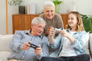 Evde mutlu bir aile. Yaşlı adam büyükbaba kadın büyükanne kız torun evde joysticklerle oyun oynuyor. Oyun için gamepad kullanan iki nesil büyükbaba ve ergen