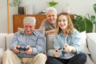 Evde mutlu bir aile. Yaşlı adam büyükbaba kadın büyükanne kız torun evde joysticklerle oyun oynuyor. Oyun için gamepad kullanan iki nesil büyükbaba ve ergen