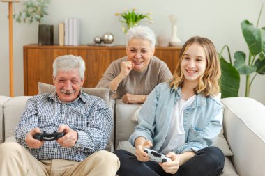 Evde mutlu bir aile. Yaşlı adam büyükbaba kadın büyükanne kız torun evde joysticklerle oyun oynuyor. Oyun için gamepad kullanan iki nesil büyükbaba ve ergen