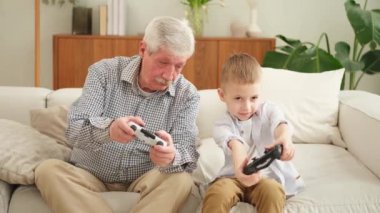 Mutlu bir aile. Yaşlı büyükbaba oğlan torun evde joysticklerle oyun oynuyor. Oyun için oyun bloknotları kullanarak gülümseyen büyükanne ve çocuk. Eski nesil modern teknoloji kullanımı