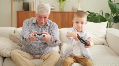 Mutlu bir aile. Yaşlı büyükbaba oğlan torun evde joysticklerle oyun oynuyor. Oyun için oyun bloknotları kullanarak gülümseyen büyükanne ve çocuk. Eski nesil modern teknoloji kullanımı